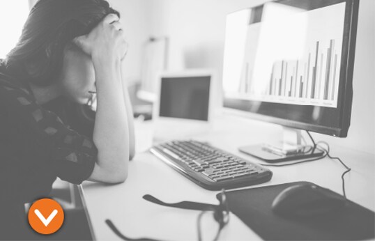 Adult holding head in hands, in front of a computer